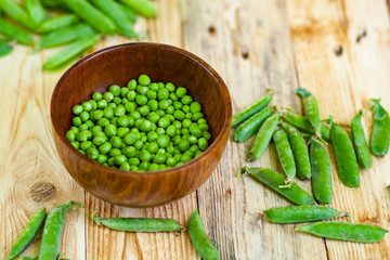 closeup green peas in brown dish, on wooden table.