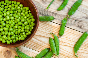 closeup green peas in brown dish, on wooden table.