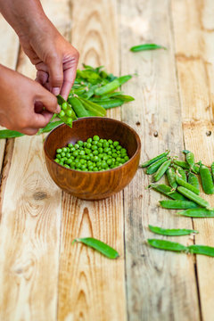 closeup of woman hand depod green peas in brown dish, on wooden table.