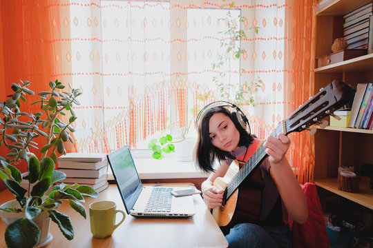 Female self education online. Woman plays guitar at front of laptop