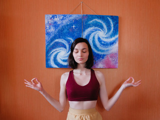 Young woman meditates on background of a galaxy painting. Home meditation concept