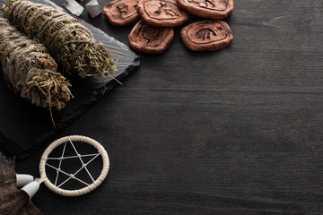Herbal smudge sticks, dreamcatcher and clay amulets on dark wooden background