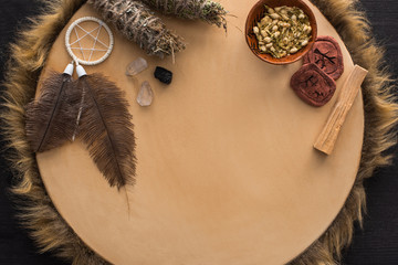 Top view of smudge sticks with dry flowers, dreamcatcher and clay amulets on tambourine on dark...