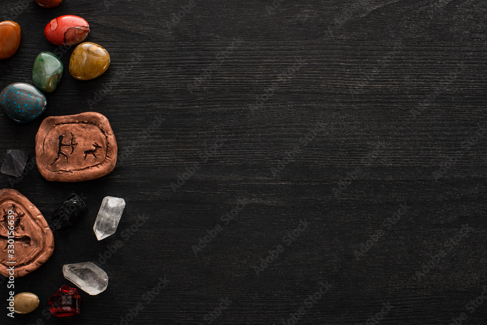 Poster top view of fortune telling stones, clay amulets and crystals on black wooden background