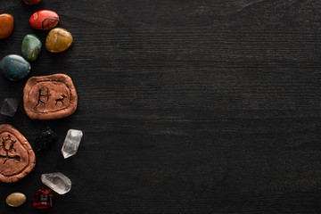 Top view of fortune telling stones, clay amulets and crystals on black wooden background