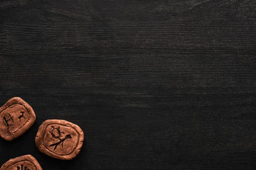 Top view of clay amulets with symbols on black wooden background with copy space