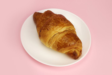 croissant in a white plate on a pink, colored background