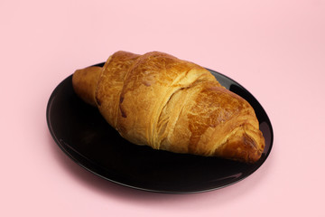 croissant in a black plate on a pink, colored background