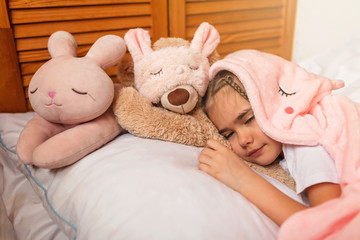 Fototapeta na wymiar Top view of cute awaking girl with her toy animals wearing in light pink pajama with unicorn hoody