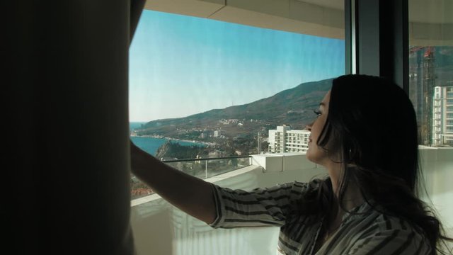 woman opens the curtains , a window with a view of the sea