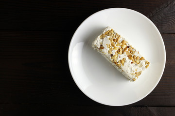 Pieces of sherbet or nougat with nuts in a plate on a dark wooden background