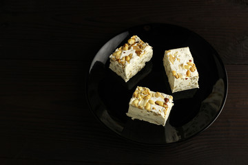 Pieces of sherbet or nougat with nuts in a plate on a dark wooden background