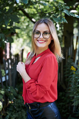 Close-up portrait of attractive young woman with short blond hair, wearing eyeglasses, smiling in the summer garden, Happy female student, posing in the park. Sunny day in campus.