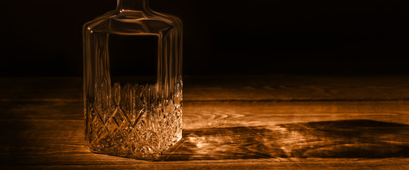 An elegant empty carafe, on a textured wooden table. Decanter in dark style.
