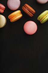 Macaroni cookies of different colors lie on a black textured background. Free space. Still life of confectionery.