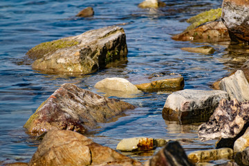 Large and smooth stones in the coastal waves of salty sea water. The coast of the black sea foams and roars, beating against a huge pebble, illuminated by sunlight