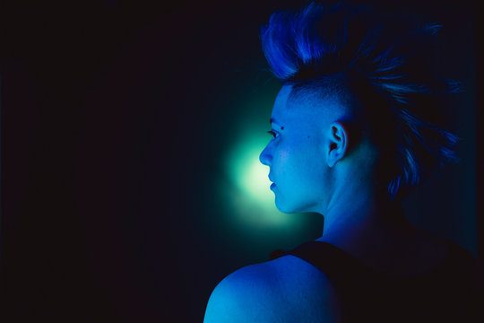 Bisexual people and gay pride. Lgbt concept. Strong androgynous female with non binary gender. Portrait of a punk lesbian woman with a mohawk blue hairdo. Isolated gay woman on green background. - Powered by Adobe