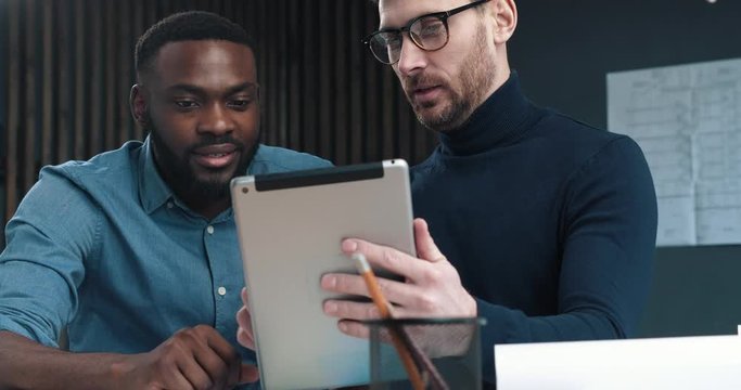 Close Up of two modern experienced Business Men working on PC Tablet. Two stylish Engineers are working concentrated in the dark blue Office, working in team. Construction Company. Architects.