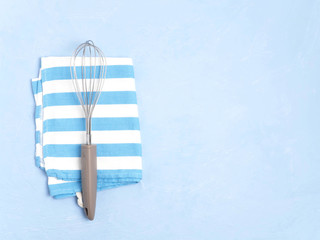 Whisk and towel on a blue concrete background.