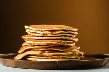 Stack of pancakes on a wooden plate. Copy space for your text.On a light brown background.