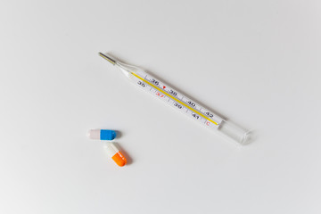 Thermometer and two capsules of orange and blue on a white table