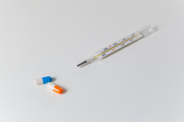 Thermometer and two capsules of orange and blue on a white table