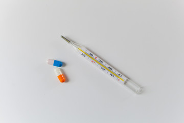 Obraz premium Thermometer and two capsules of orange and blue on a white table