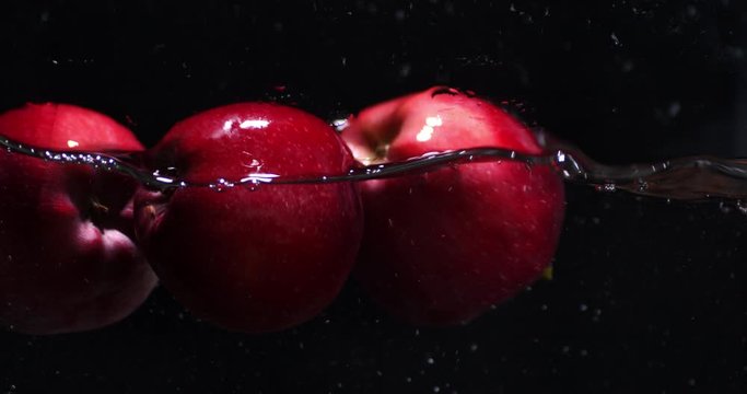 Red fresh apples fall into the water.