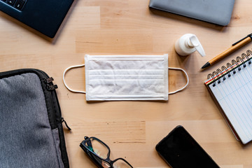 remote work kit on wooden office desk with hand sanitizer and face mask, a solution against the spread of corona virus for quarantined employees