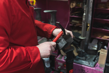 Detail of a shoemaker's hands dressed in red working with a hammer and shoes
