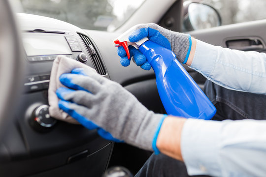 Man cleansing car dashboard and spraying with disinfection liquid.