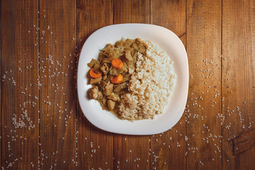 arroz frito con pollo y verduras. zanahoria, judías verdes. En plato blanco, fondo de madera.
