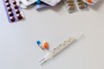 A large number of drugs on a white background next to a thermometer and two capsules of orange and blue