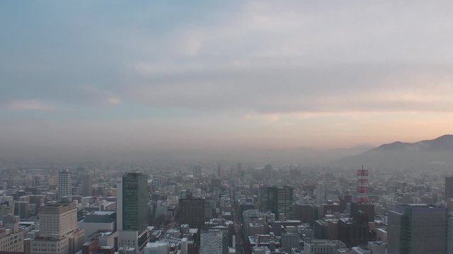 SAPPORO, HOKKAIDO, JAPAN - FEB 2020 : Aerial high angle sunset view of cityscape of Sapporo city. View of buildings and street traffic around Susukino downtown area. Time lapse shot sunset to night.