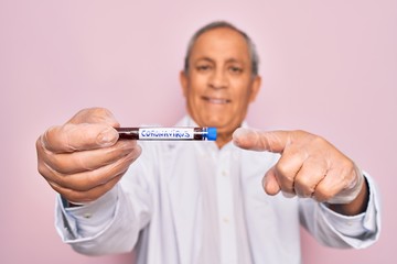 Senior handsome hoary man holding coronavirus tube test over isolated pink background very happy pointing with hand and finger