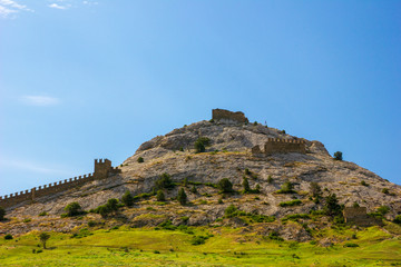 Fototapeta na wymiar An ancient fortress on top of a mountain against a sunny blue sky. Genoese fortress, Sudak, Crimea. Historic old building. Monument of architecture.