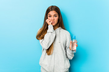 Young fitness woman holding a water bottle biting fingernails, nervous and very anxious.