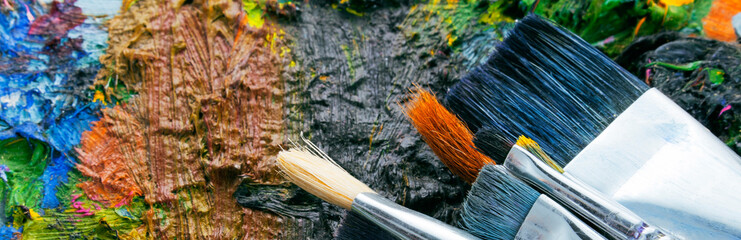 Closeup of art palette with colorful mixed paints and paintbrushed. Panorama. 