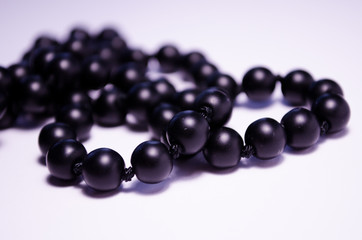 Shungite. Black beads on a white background. Photography for jewelry stores, fashion boys, style. Handwork. Matte black round mineral on a white background. Decoration of natural stones (necklace).