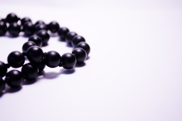 Shungite. Black beads on a white background. Photography for jewelry stores, fashion boys, style. Handwork. Matte black round mineral on a white background. Decoration of natural stones (necklace).