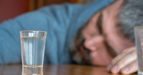 drunk man sleeps falling on table with glass of vodka in alcoholic intoxication