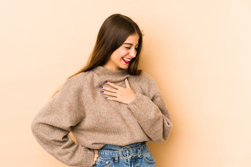 Young caucasian woman isolated en beige background laughing keeping hands on heart, concept of happiness.
