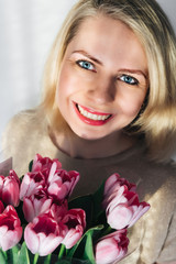 portrait of a beautiful girl with fresh flowers on a light background. a young blonde woman in light clothing looks straight ahead