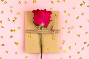 Vintage gift packing in eco paper with stars glitter sprinkles on soft pink background. Present decorated with rose flowers. Birthday, Mother's, Valentines, Wedding Day concept, top view, flat lay