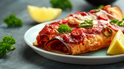Baked Chicken fillets enchiladas with courgette, salsa sauce and cheese served with lemon wedges and chilies