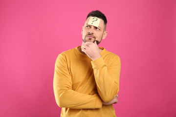 Emotional man with question mark on pink background