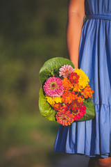 A young girl in a blue dress holds in her hand a beautiful bouquet of wildflowers on a sunny day. A bouquet of colorful flowers in a woman's hand. Toning