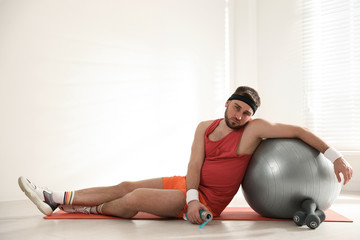 Lazy young man with sport equipment on yoga mat indoors. Space for text