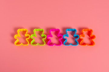 multi-colored plastic cookie cutters for making cookies in the form of a teddy bear on a pink background. Culinary concept. Flat lay with copyspace.