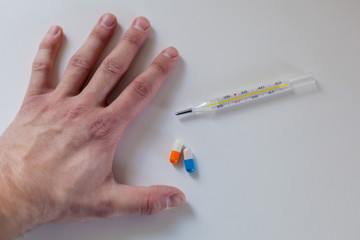 Male hand on white table. Next to a thermometer and two pills